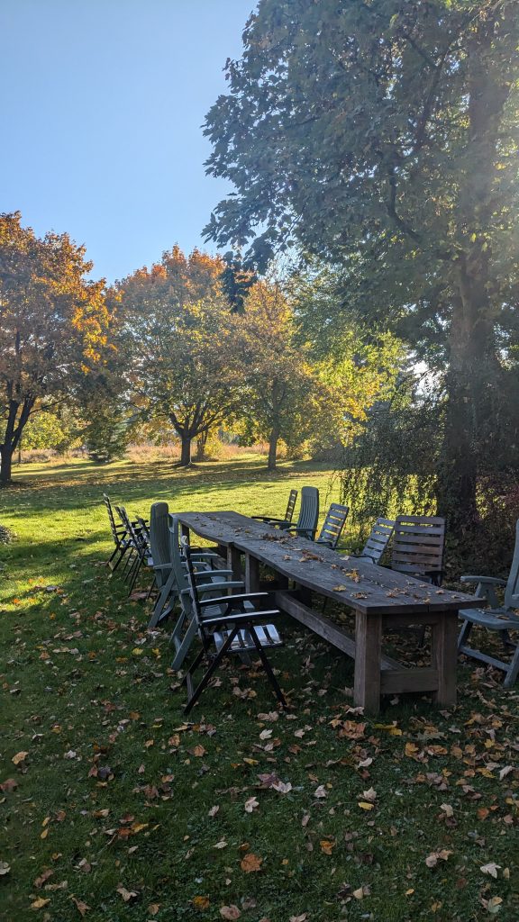 herbstlicher Garten mit langem Holztisch und vielen Stühlen